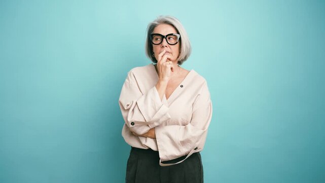 Pensive senior woman with grey hair and glasses thinking, then finding a solution and celebrating with a eureka moment against a blue background