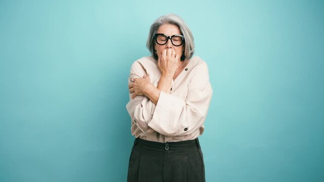 Senior woman with grey hair feeling very cold and shivering, hugging herself for warmth. Anxious lady suffering from low temperature