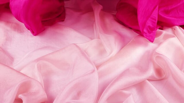 Pink silk fabric falling down on textile background in slow motion. This video is perfect for fashion branding. Bright magenta and soft rose materials create a premium look for luxury cosmetics.