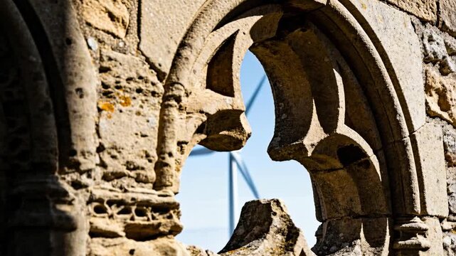 Shifting camera bringing three-blade turbine into stone tracery at ruin to center energy contrast