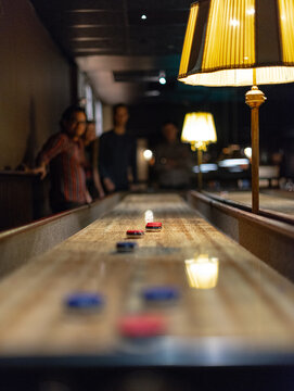 Friends playing shuffleboard in cozy dimly lit bar interior.
