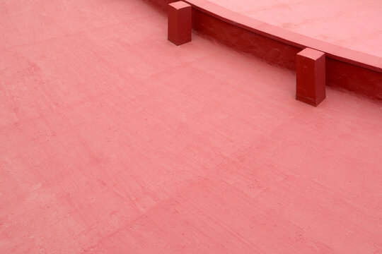 A vibrant red painted flat rooftop surface with two small concrete pillars features minimal geometric design elements and copy space.