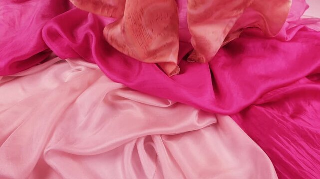 Peach silk fabric gently falls onto orange and pink scarfs. Elegant drape showcases smooth texture. Soft coral, terracotta, and fuchsia materials create ideal background for premium fashion.