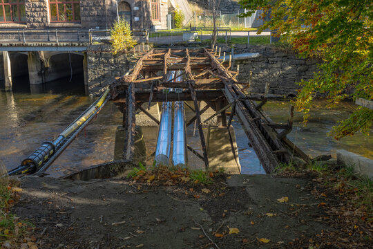 Rusted bridge structure with exposed metal pipes over river.