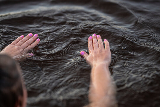 Hands with pink nails floating gently on dark rippling water.