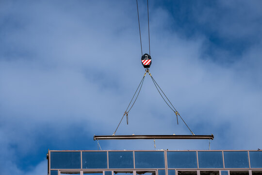 Construction crane lifting steel beam above modern building under blue sky.