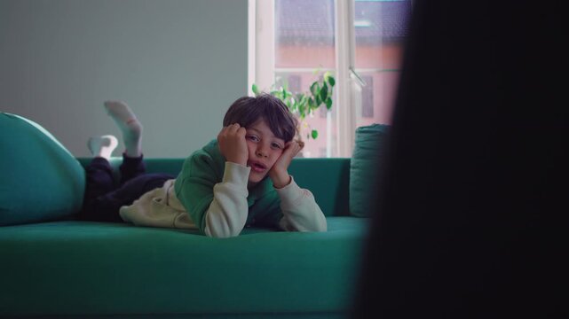 Boy resting on sofa while absorbed in off screen digital media, authentic childhood moment highlighting screen engagement, entertainment habits and contemporary family life