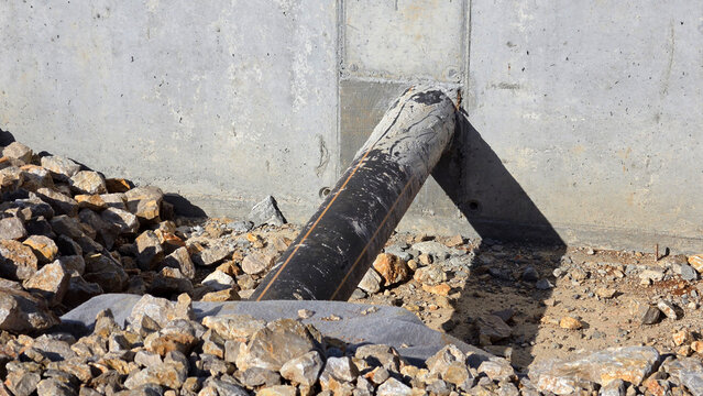 Black plastic utility pipe protruding from concrete wall into rocky ground