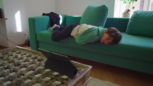 Young child captivated by tablet screen while lying on couch, contemporary family scene expressing attention, media engagement and digital entertainment habits