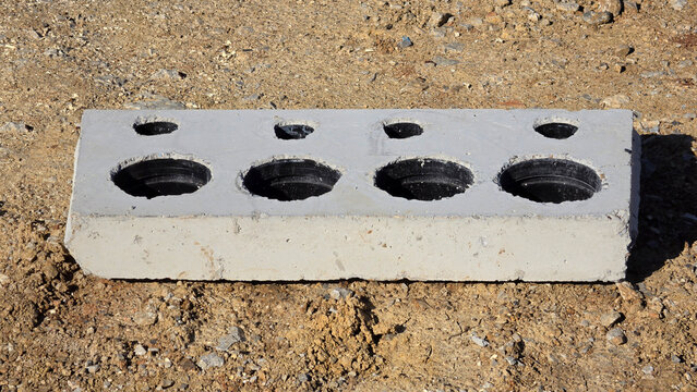 Precast concrete lintel wall panel with integrated circular plastic conduit knockouts on dirt ground