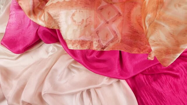 Soft silk fabric falls gently in slow motion onto coral and fuchsia textiles. Elegant drapery creates a fluid abstract background. High-quality texture is ideal for beauty industry advertising.