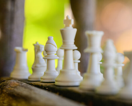 Artistic close up of white chess king and pieces on rustic board with soft lighting.