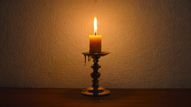 Candle burning centered close-up on brass holder, single flame against plain wall for memorial tribute, funeral prayer, power outage, spiritual service, condolence message, and remembrance ritual