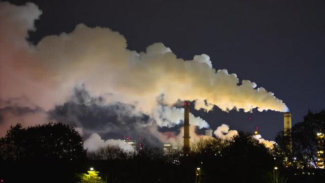 Factory emitting wide night view with smoke plume above industrial skyline, power plant stacks and pollution haze for climate reporting, air quality alerts, energy policy, and public health warnings