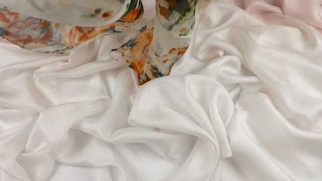 Vintage floral silk scarf gently falls onto soft white fabric. Organic movement of the textile creates a luxurious backdrop. Elegant orange roses on cream satin add a premium aesthetic to projects.
