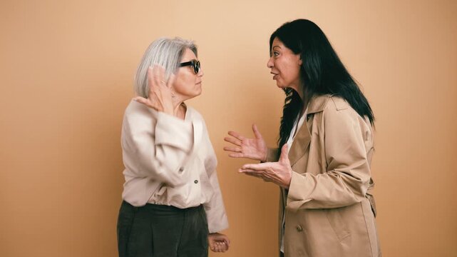 Two stylish middle aged women are having a very animated discussion. They gesture intensely, shouting at each other until they finally burst out laughing