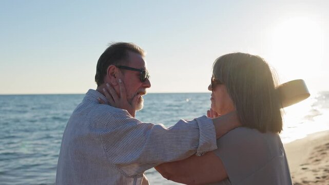 Happy senior couple showing affection and love while smiling together on a sandy beach during a beautiful, sunny evening, enjoying their retirement vacation by the sea with ukelele and music