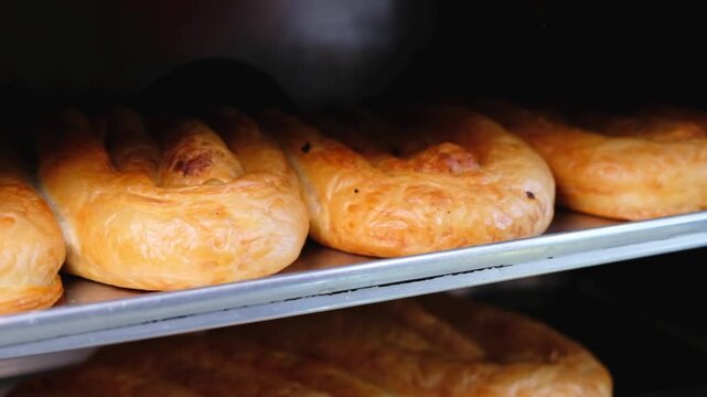 Close-up footage of freshly baked b&ouml;rek resting on a metal oven tray, showing golden crispy pastry layers, traditional Turkish food preparation and hot bakery service.