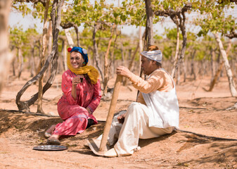 Fototapeta premium Authentic Middle Eastern couple in vibrant traditional embroidered clothing relaxing together with tea during agricultural work break in sunny sandy