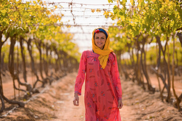 Obraz premium Confident Middle Eastern woman farmer in colorful traditional embroidered pink dress and yellow headscarf walking directly toward camera through