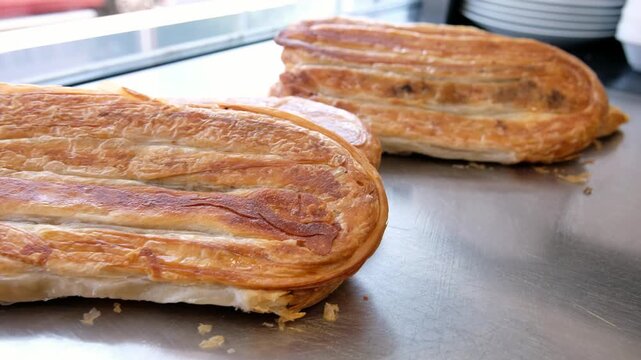 Close-up footage of freshly baked b&ouml;rek with golden crispy layers on a kitchen counter, showing traditional Turkish pastry, savory bakery food and appetizing restaurant presentation.