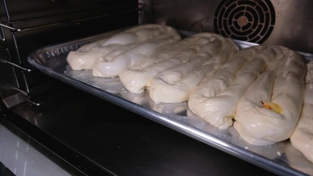 Close-up footage of raw b&ouml;rek pastries arranged on metal trays and placed inside an oven, showing traditional Turkish pastry preparation, fresh dough, bakery production and baking process.