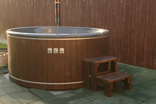 hot tub with wooden cladding and metal rim standing on patio near fence Outdoor. Hot tub filled for soaking and relaxation, hot tub creating cozy spa atmosphere in backyard, wellness lifestyle concept