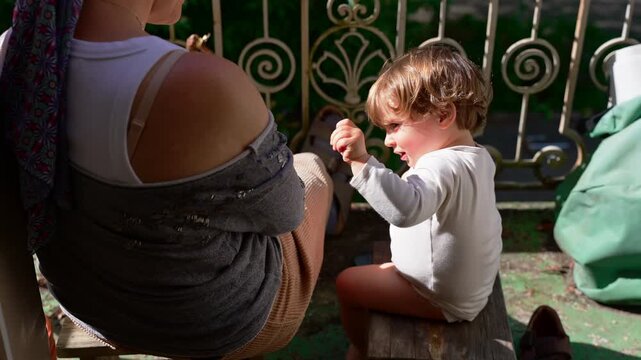 Mother and toddler sitting together on sunlit balcony, peaceful family moment as young child reaches for attention, expressing attachment, trust and emotional connection