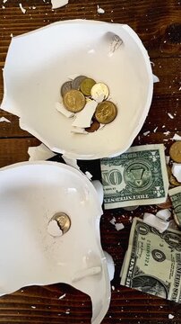 Slow motion footage of a piggy bank full of coins and dollar bills being smashed with a sledgehammer on a wooden table