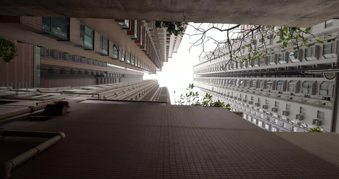 Extreme low angle panning shot from narrow back alley in Hong Kong, revealing dense urban environment with closely packed tall buildings, showcasing architectural density and vertical cityscape.