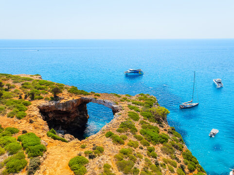 Aerial view of Cala Varques beach bay and turquoise sea in Mallorca, Spain. Scenic coastline landscape with boats and yachts in summer. Mediterranean nature and vacation destination from drone.