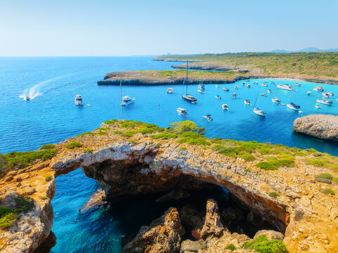 Aerial view of Cala Varques beach bay and turquoise sea in Mallorca, Spain. Scenic coastline landscape with boats and yachts in summer. Mediterranean nature and vacation destination from drone.