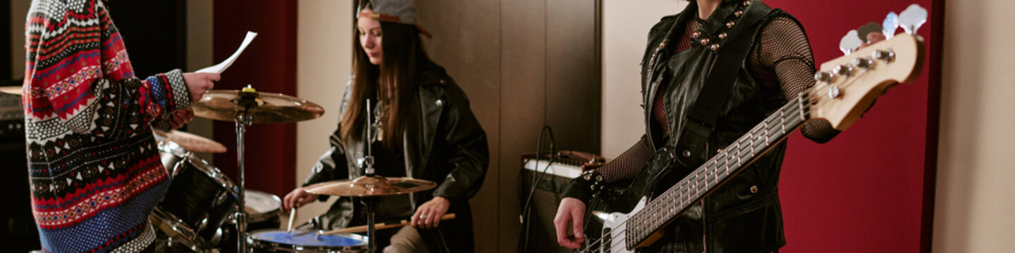 Header of teenage girls music group rehearsing with drums and bass guitar in studio, performing teamwork and creative practice. Useful for youth band promotion, music education marketing