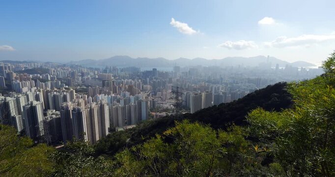 Panoramic view from high hillside trail overlooking Kowloon dense urban landscape, dominated by towering residential high-rises. Intensity of new high-rise housing estates and widespread urban sprawl
