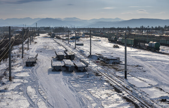 Aerial view of a snow-covered railway yard with freight trains, concrete sleepers, and distant mountains in Severobaykalsk, Buryatia, Russia.