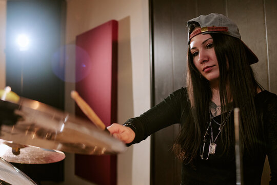 Young adult woman drummer playing cymbals in recording studio, performing with focus for girls music group promotion. Medium shot, fitting band marketing, youth culture, entertainment campaigns