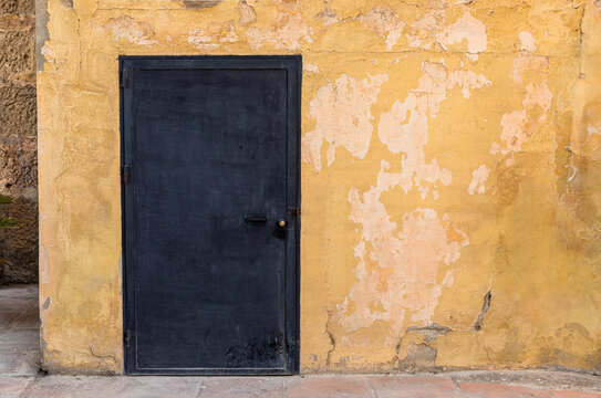 Old ochre textured wall with black door
