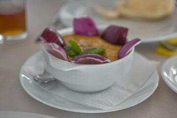 A bowl of traditional Canarian gofio escaldado topped with raw red onion slices and fresh mint leaf garnish on a restaurant table in Gran Canaria. © Javier