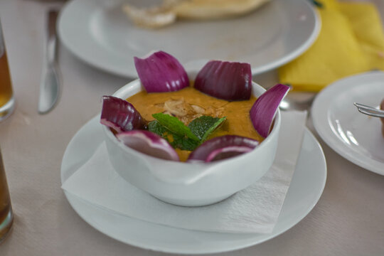 High-angle view of traditional Canarian gofio escaldado served in a white bowl, garnished with fresh red onion petals and mint on a restaurant table.