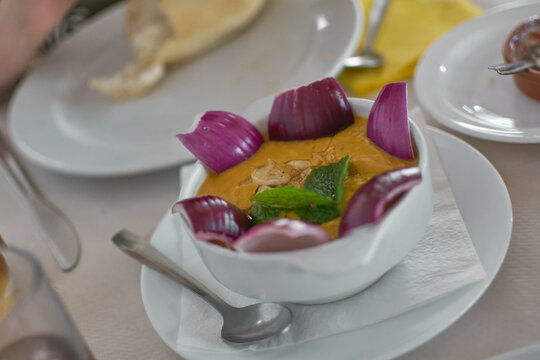 A traditional bowl of Canarian gofio escaldado served with fresh red onion wedges and mint garnish on a restaurant table in Gran Canaria.