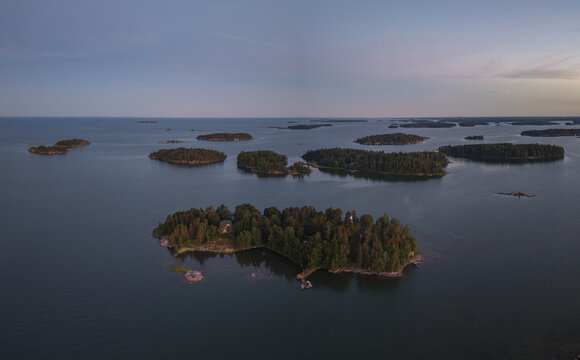Aerial view of the Baltic Sea archipelago featuring small forested islands surrounded by calm waters under a soft evening sky in Espoo, Uusimaa, Finland.