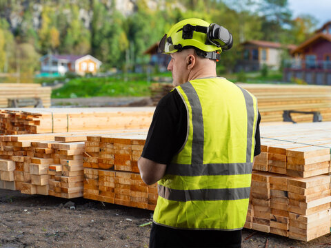 Timber construction, Site worker inspects stacked lumber for house building and carpentry supply at outdoor work area