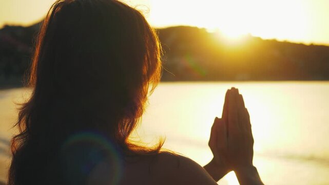 Woman embodying serenity and spiritual connection in prayer pose at sunset by the water, radiating inner peace and calmness, perfect for mindfulness and wellness marketing.