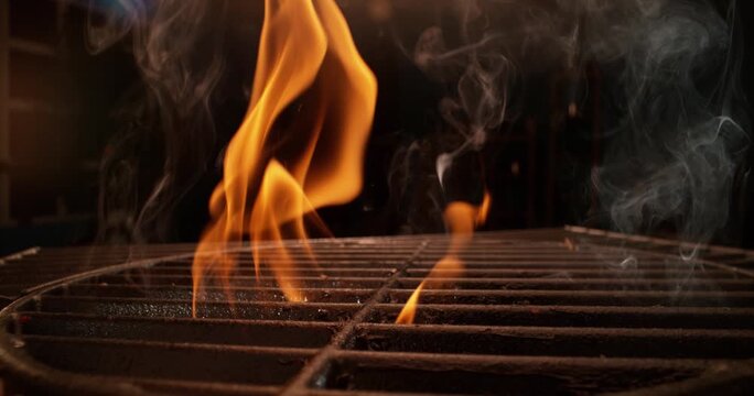 Fire flames and swirling smoke rising from cast iron barbecue grill grate at night.