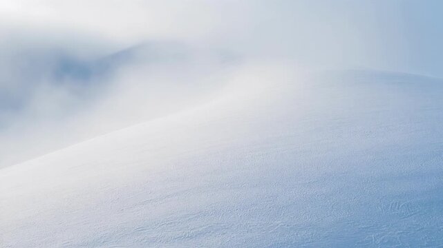 Smooth snow-covered hill under a pale blue sky with soft clouds