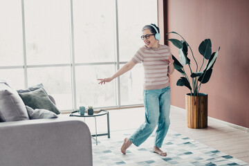 Senior woman dancing happily at home while wearing headphones in a bright modern living room