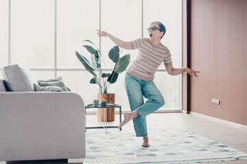 Joyful senior woman dancing barefoot in bright living room, playful home lifestyle and carefree moment