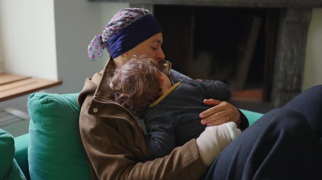 Mother recovering from cancer embracing toddler on sofa at home, family support moment highlighting healing, resilience, attachment and emotional strength