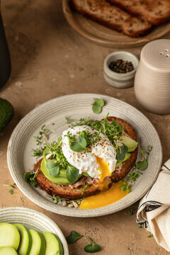 Healthy avocado and poached egg toast sprinkled with microgreens on beige textured background. Healthy morning breakfast