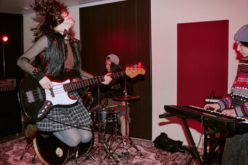 Teenage girls performing in music group, playing bass guitar, drums, keyboard during rehearsal or...